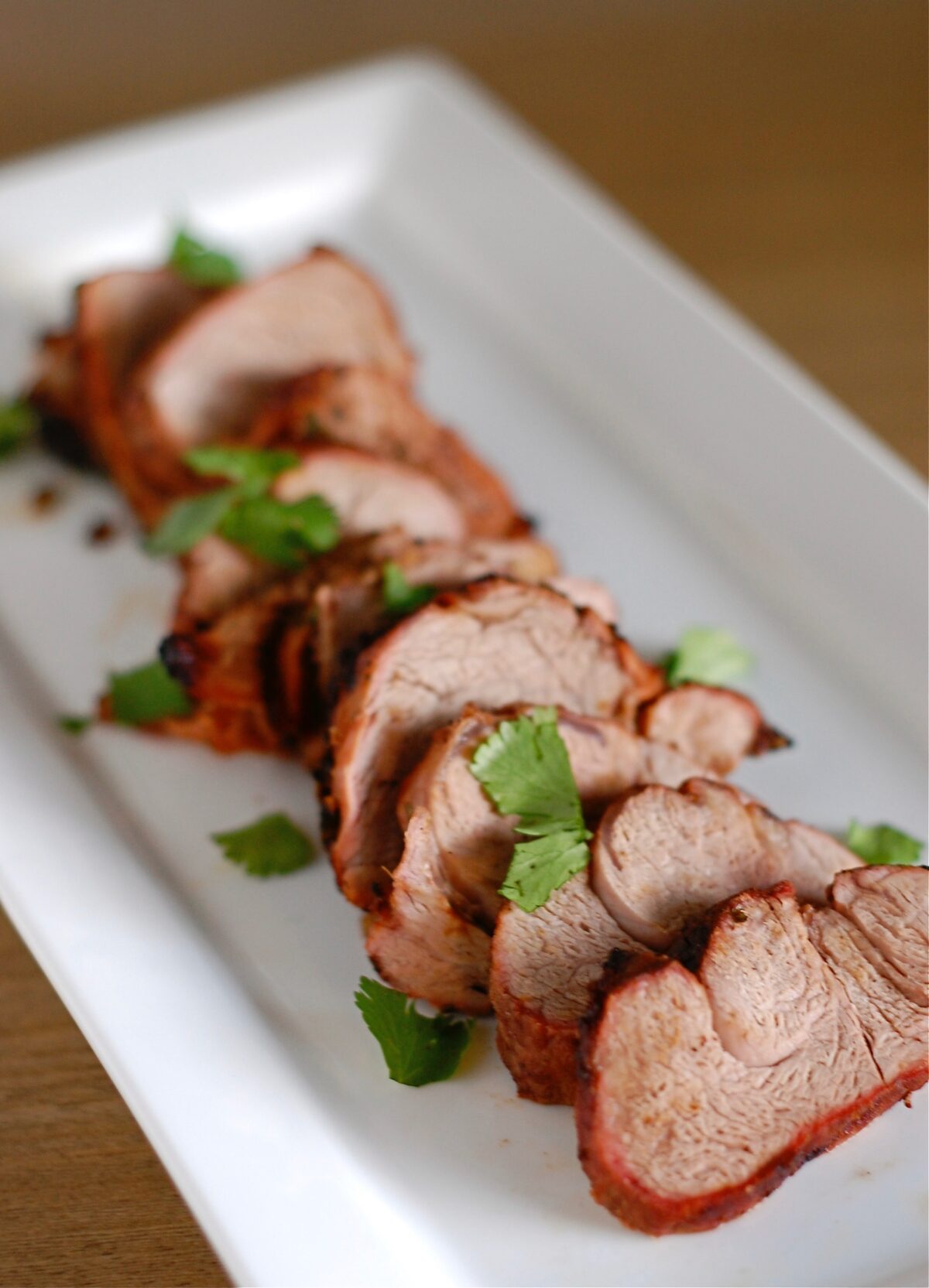 pork tenderloin sliced on a white plate topped with fresh cilantro.