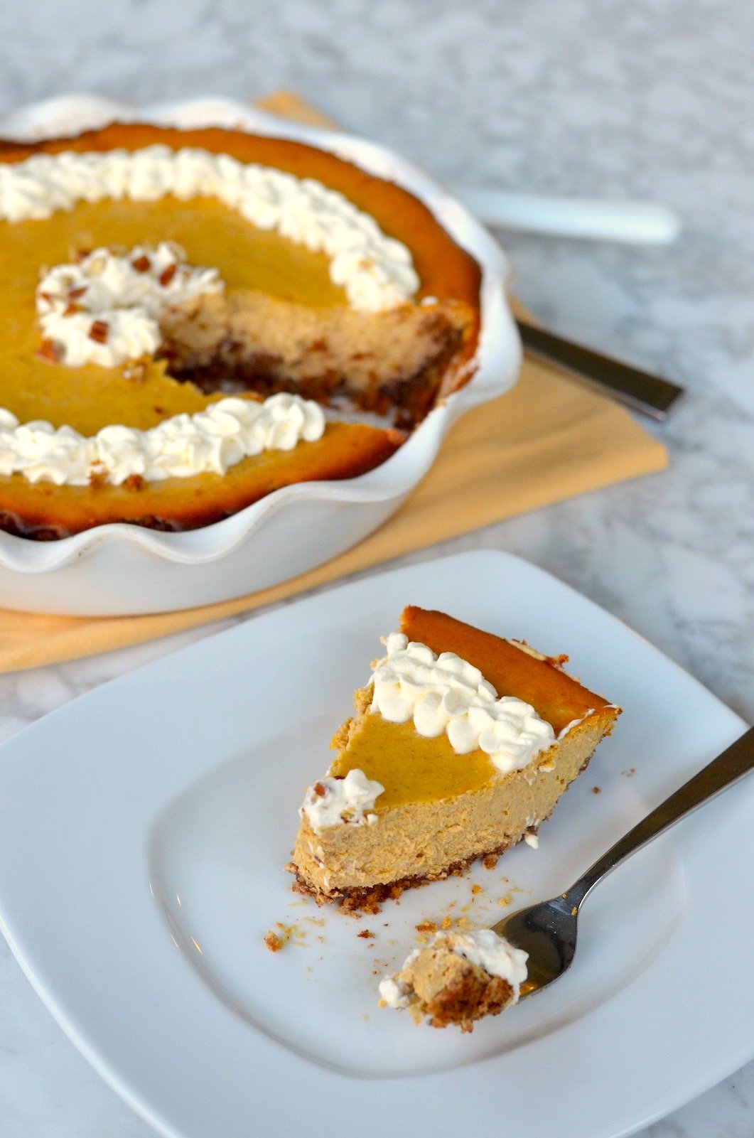 Pumpkin Cheesecake in a pie dish in the background with one piece on a plate in front with whipped cream on top.