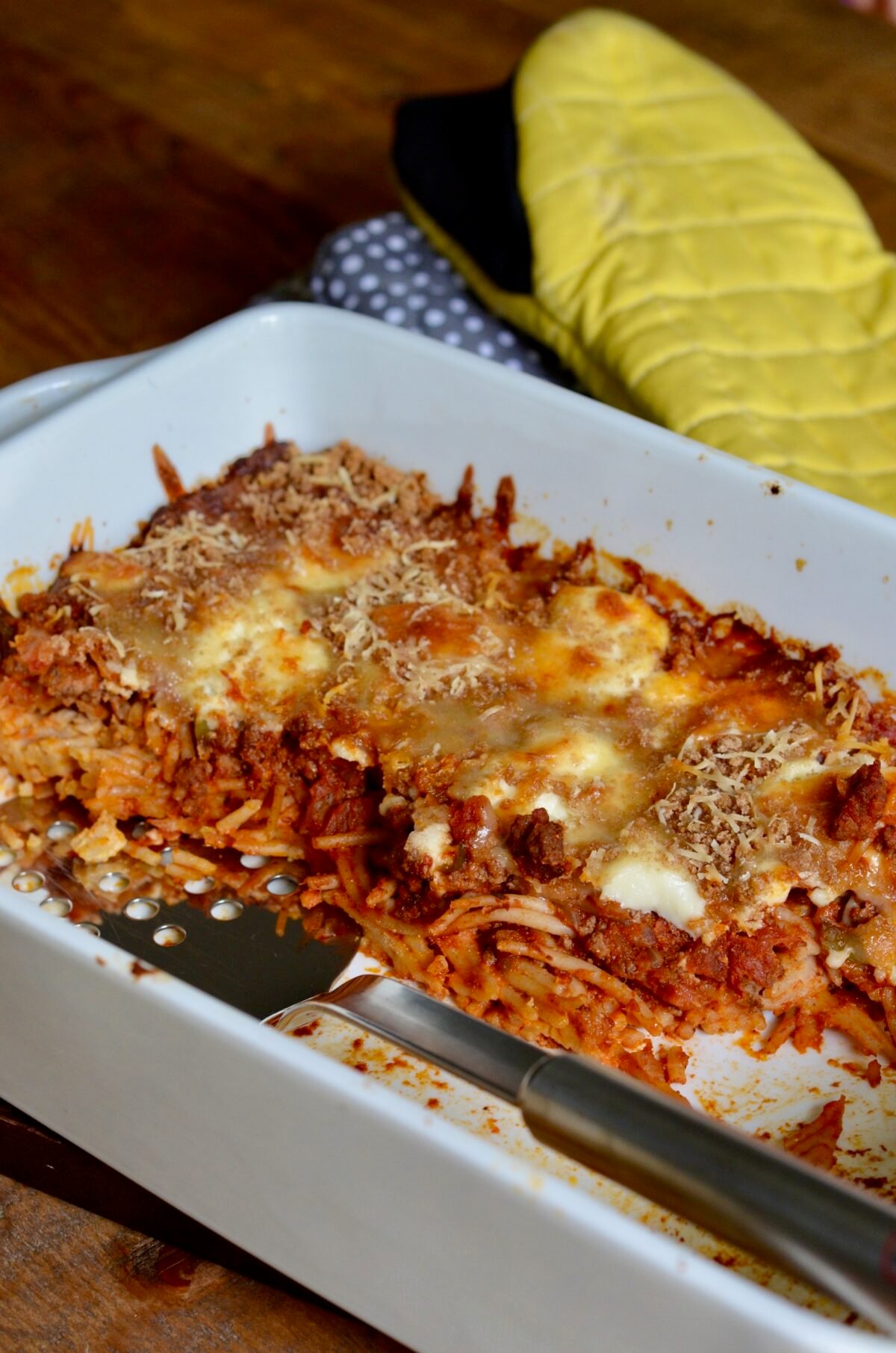 Homemade baked spaghetti casserole in a white baking dish half eaten.